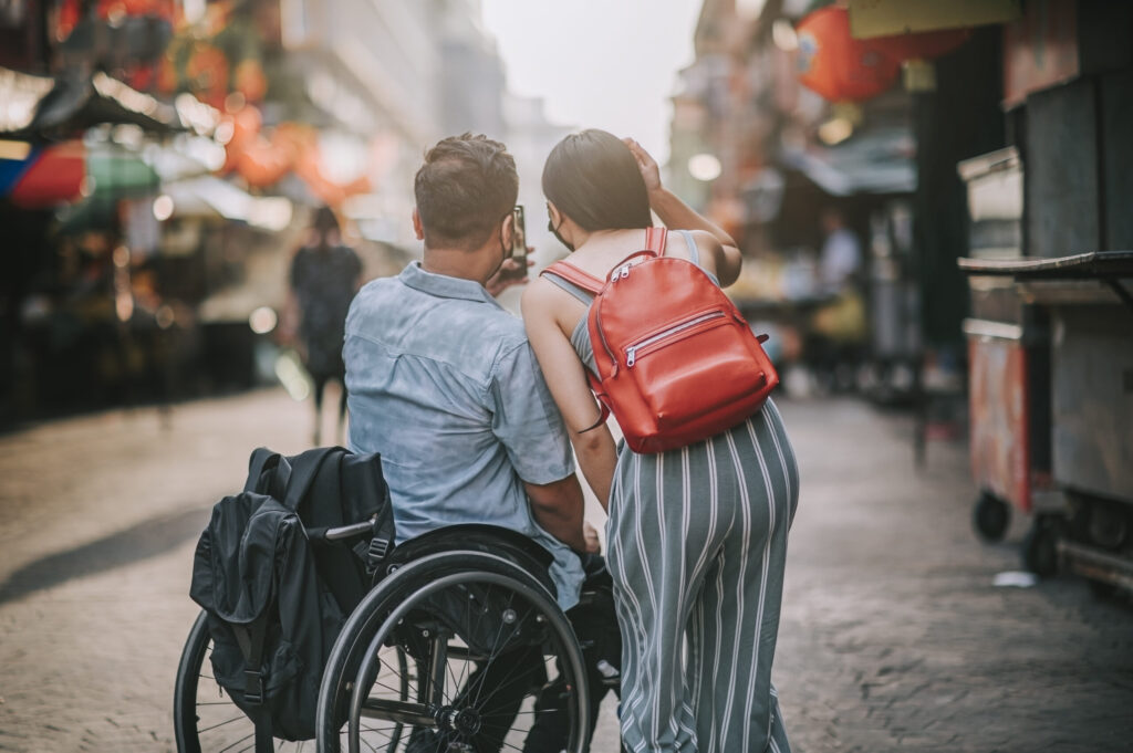 rear view tourist asian chinese couple with wheelchair photographing using smart phone at petaling street, kuala lumpur during sunset