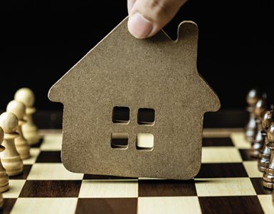 Close up of a hand making a chess move with a house as it's player piece.
