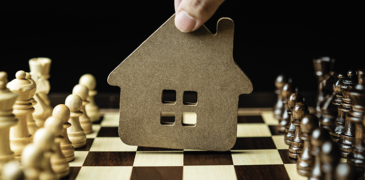 Close up of a hand making a chess move with a house as it's player piece.