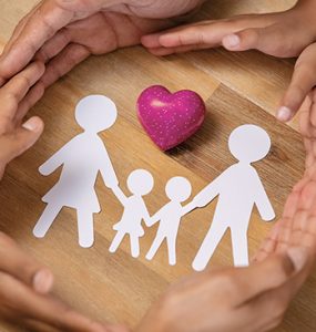 A family linking hands around heart and paper cut-out of family unit.