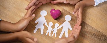 A family linking hands around heart and paper cut-out of family unit.
