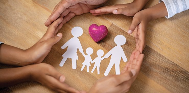 A family linking hands around heart and paper cut-out of family unit.