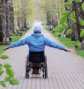 A man in his wheelchair whith his arms outstretched surrounded by a beautiful green park.