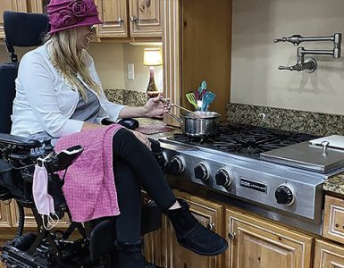 A woman who uses a raised wheelchair is cooking on her stove.