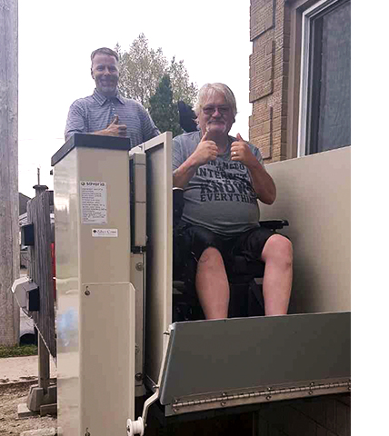 Robert in wheelchair lift with John from Silver Cross behind him