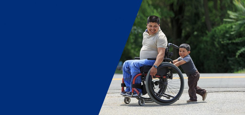 Young father in a wheelchair being pushed by his young son.