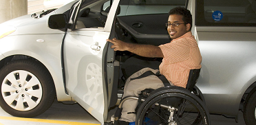 Man in wheelchair getting into driver's side of car