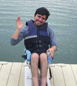 A young man sit on his wakeboard on a dock overlooking a large ontario lake.