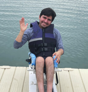 A young man sit on his wakeboard on a dock overlooking a large ontario lake.