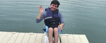 A young man sit on his wakeboard on a dock overlooking a large ontario lake.