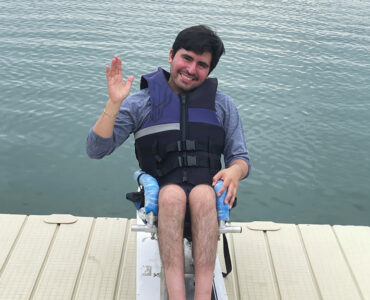 A young man sit on his wakeboard on a dock overlooking a large ontario lake.