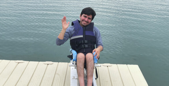 A young man sit on his wakeboard on a dock overlooking a large ontario lake.