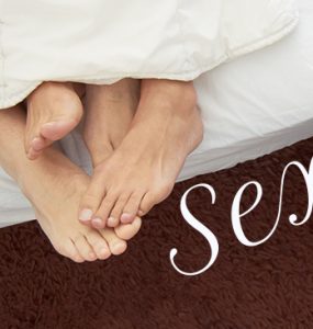 A couple's feet hanging off the bottom of a bed and a wheelchair is parked bedside.