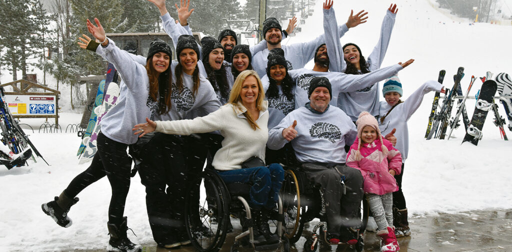 A group of sit-skiers and Ski Day participants throw their hands up in joy for the group photo.