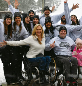 A group of sit-skiers and Ski Day participants throw their hands up in joy for the group photo.
